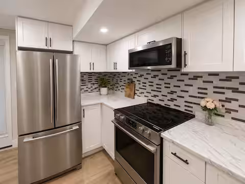 Kitchen with white cabinets, stove, microwave and refrigerator